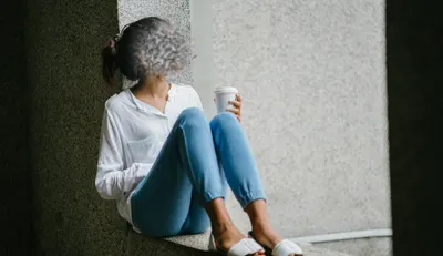 A girl sitting calmly with a cup in hand on a wall bench