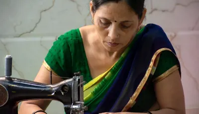 A woman tailoring fabric as part of a livelihood training program using natural and discarded materials.