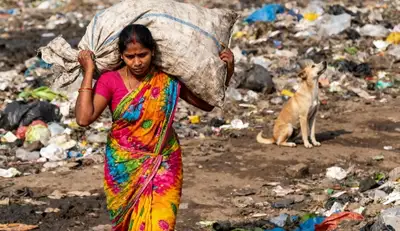 A woman carrying waste on her back from a dumpyard